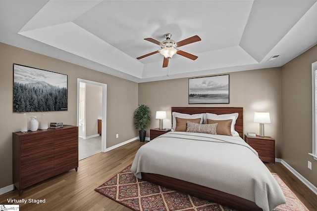 bedroom with a tray ceiling, wood finished floors, visible vents, and baseboards