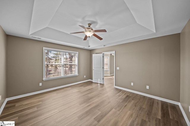 unfurnished bedroom featuring ceiling fan, wood finished floors, visible vents, baseboards, and a raised ceiling