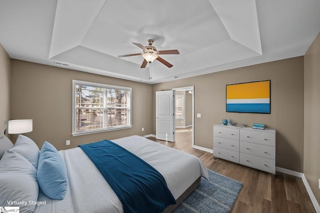 bedroom featuring a raised ceiling, visible vents, baseboards, and wood finished floors