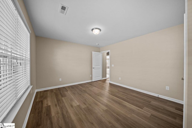 unfurnished room with plenty of natural light, wood finished floors, visible vents, and baseboards