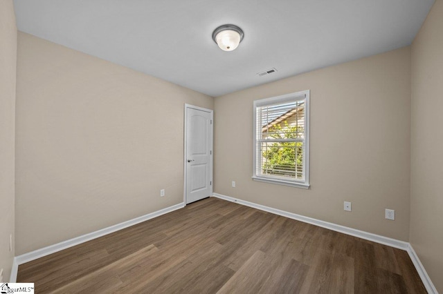 spare room with baseboards, visible vents, and wood finished floors