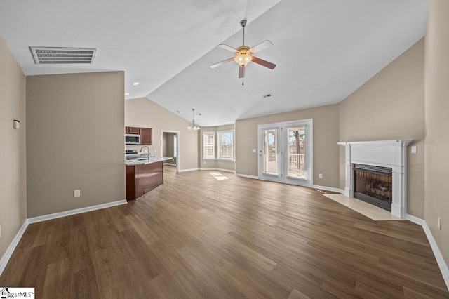 unfurnished living room with visible vents, lofted ceiling, a fireplace with flush hearth, wood finished floors, and ceiling fan with notable chandelier