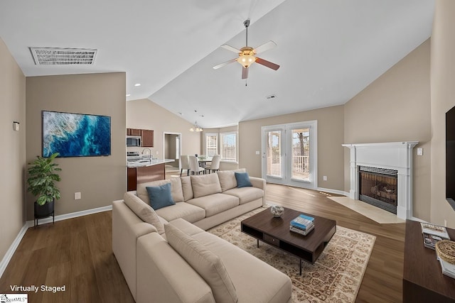 living area featuring a fireplace with flush hearth, visible vents, vaulted ceiling, and wood finished floors