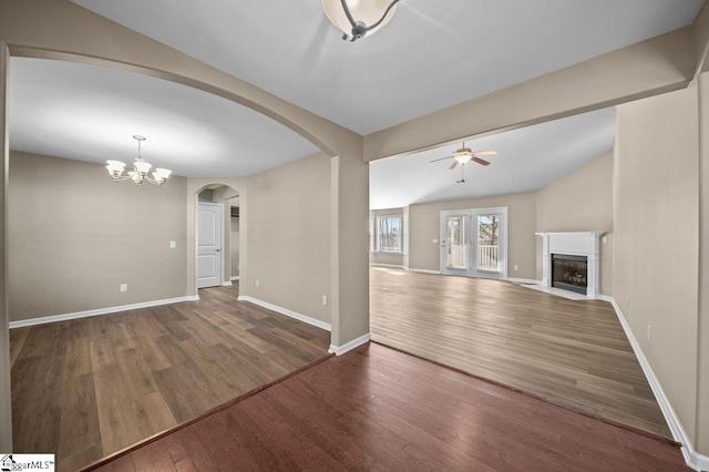 unfurnished living room featuring a fireplace with flush hearth, arched walkways, baseboards, and wood finished floors