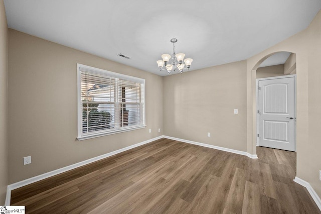 spare room featuring arched walkways, wood finished floors, visible vents, baseboards, and an inviting chandelier