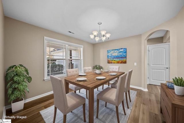 dining area featuring a notable chandelier, light wood finished floors, arched walkways, and baseboards