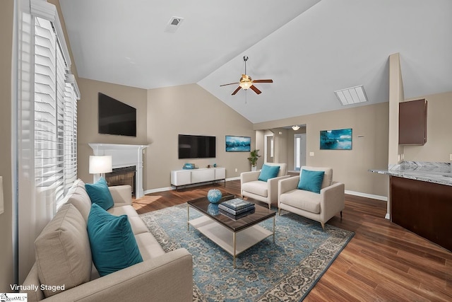 living area with lofted ceiling, a ceiling fan, a glass covered fireplace, wood finished floors, and baseboards