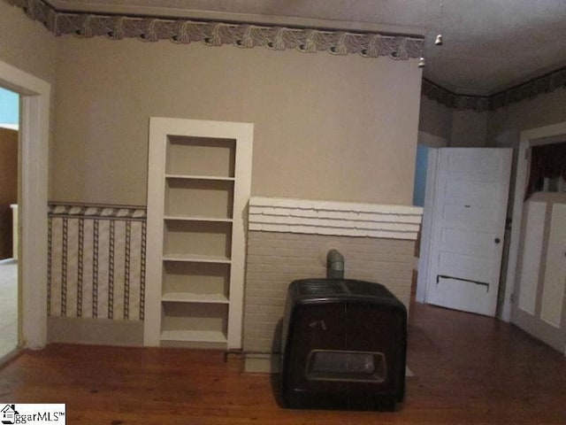 unfurnished living room featuring a wood stove, a wainscoted wall, built in features, and wood finished floors