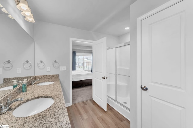 full bathroom featuring double vanity, a stall shower, a sink, and wood finished floors