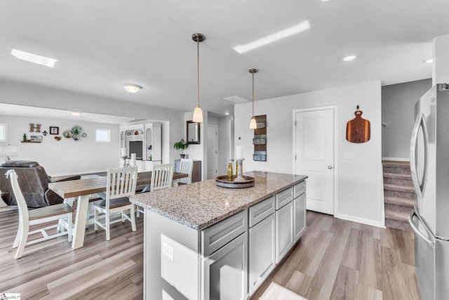 kitchen featuring light wood-style floors, light stone countertops, freestanding refrigerator, and a center island