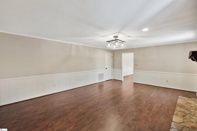 unfurnished room featuring a textured ceiling, a wainscoted wall, wood finished floors, visible vents, and ornamental molding