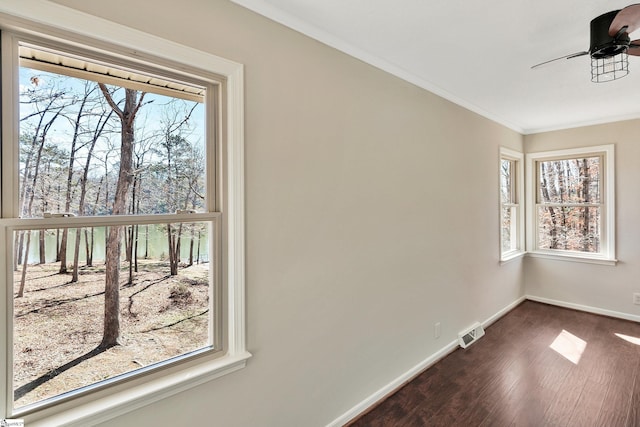 unfurnished room featuring dark wood-style flooring, visible vents, a ceiling fan, baseboards, and ornamental molding