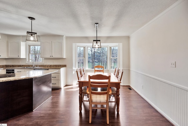 dining space featuring a wainscoted wall, visible vents, dark wood-type flooring, ornamental molding, and a textured ceiling