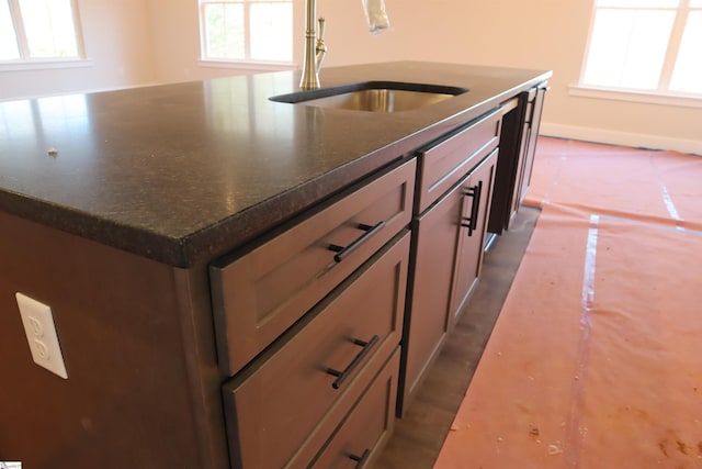 kitchen featuring plenty of natural light, baseboards, a sink, and a center island with sink