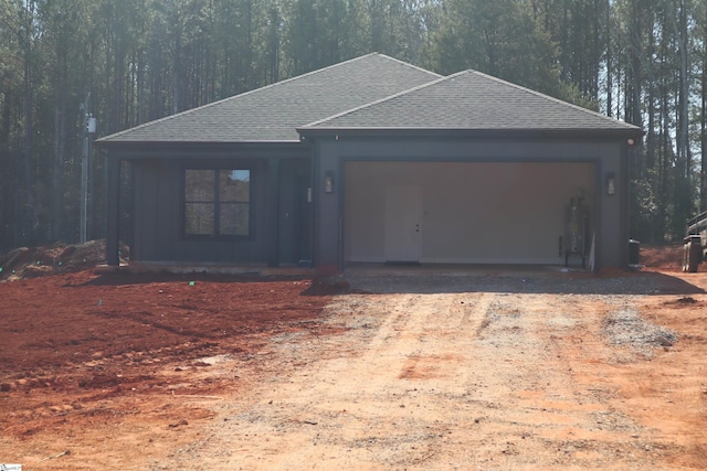 exterior space with a garage, driveway, roof with shingles, and a forest view