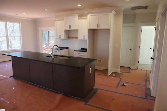 kitchen with dark countertops, visible vents, white cabinetry, a sink, and an island with sink