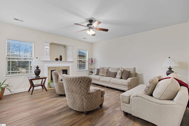 living area featuring light wood finished floors, baseboards, visible vents, a ceiling fan, and a fireplace