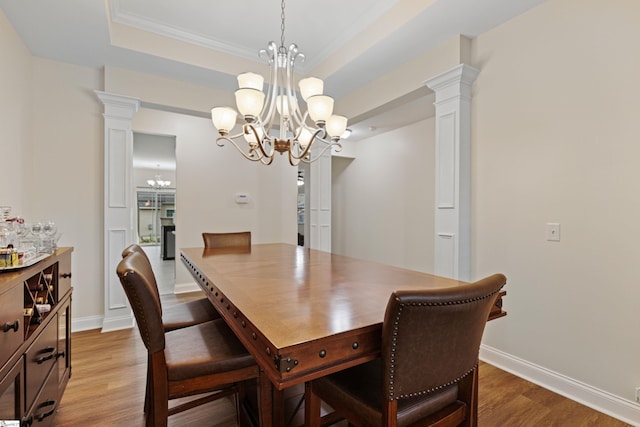 dining area featuring light wood-type flooring, decorative columns, and a raised ceiling