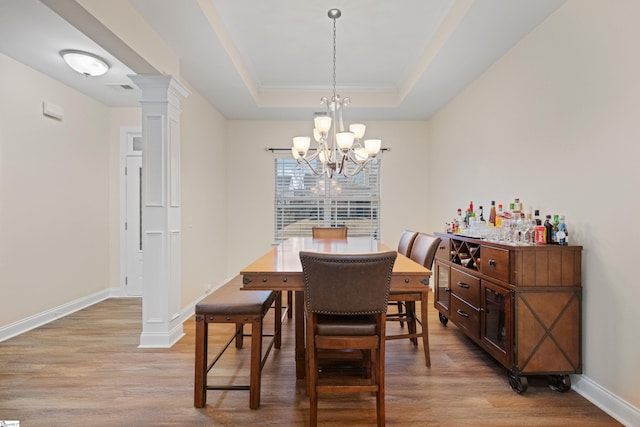 dining room featuring baseboards, a raised ceiling, decorative columns, and light wood-style floors