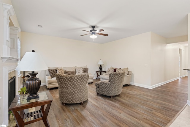 living room featuring a glass covered fireplace, ceiling fan, baseboards, and wood finished floors