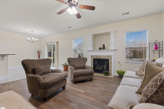 living room featuring baseboards, visible vents, a glass covered fireplace, wood finished floors, and ceiling fan with notable chandelier