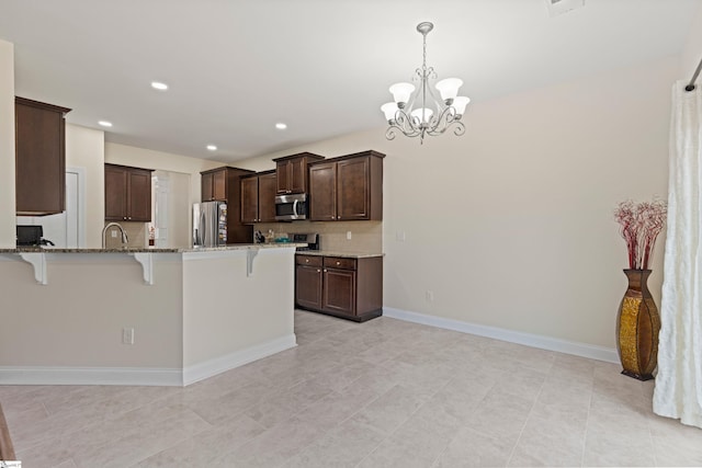 kitchen featuring dark brown cabinetry, decorative backsplash, light stone countertops, stainless steel appliances, and a kitchen bar