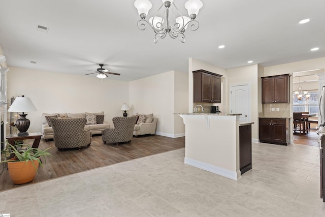 kitchen with open floor plan, dark brown cabinets, a kitchen bar, and light stone countertops