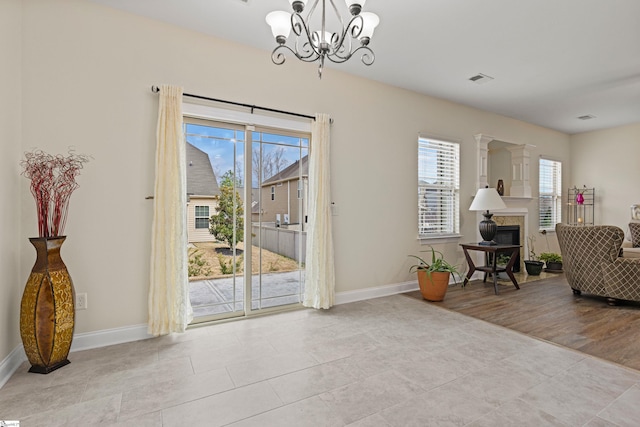 doorway to outside featuring a healthy amount of sunlight, an inviting chandelier, baseboards, and a glass covered fireplace