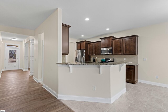 kitchen featuring appliances with stainless steel finishes, a breakfast bar, ornate columns, and light stone countertops