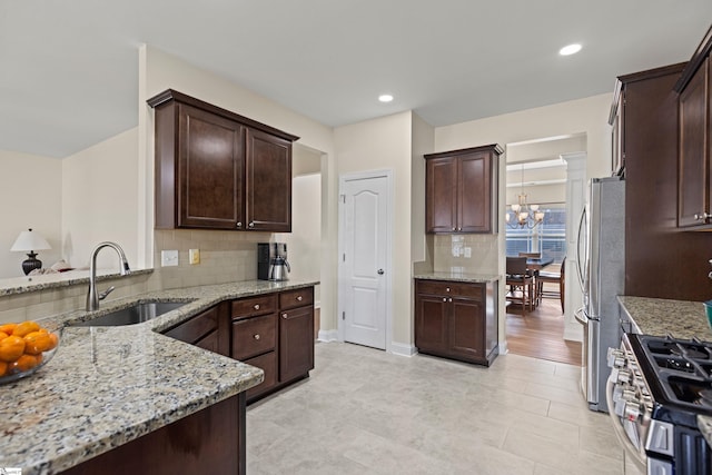 kitchen with appliances with stainless steel finishes, dark brown cabinetry, a sink, and light stone counters