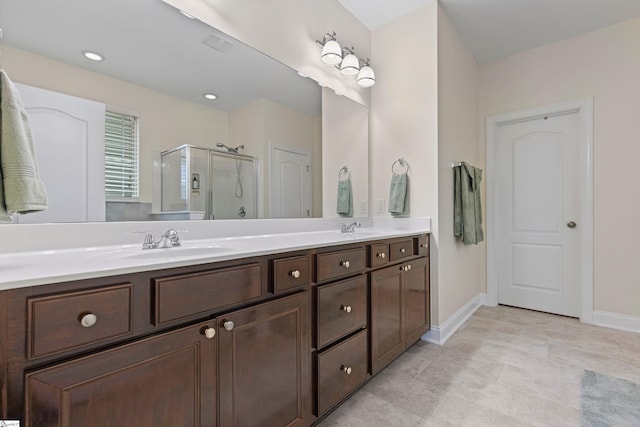 bathroom with double vanity, a shower stall, baseboards, and a sink