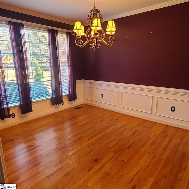 empty room with an inviting chandelier, light wood-style flooring, visible vents, and crown molding