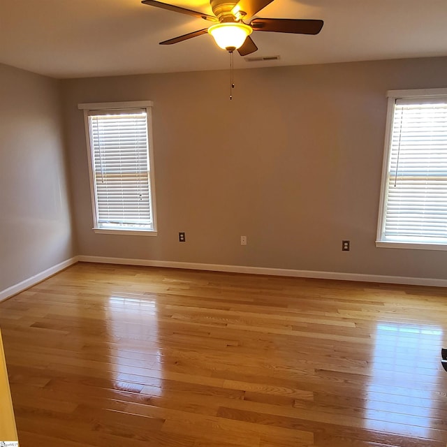 unfurnished room featuring light wood-type flooring, ceiling fan, visible vents, and baseboards