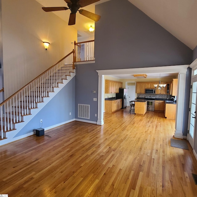 unfurnished living room featuring high vaulted ceiling, visible vents, baseboards, stairway, and light wood finished floors