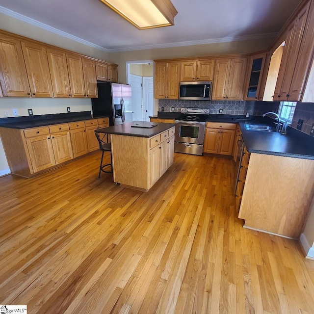 kitchen with dark countertops, appliances with stainless steel finishes, a center island, light wood-type flooring, and a sink