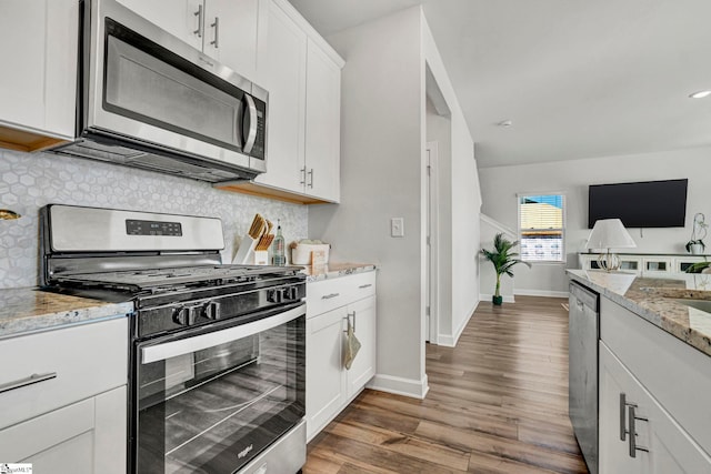 kitchen with decorative backsplash, appliances with stainless steel finishes, wood finished floors, light stone countertops, and white cabinetry