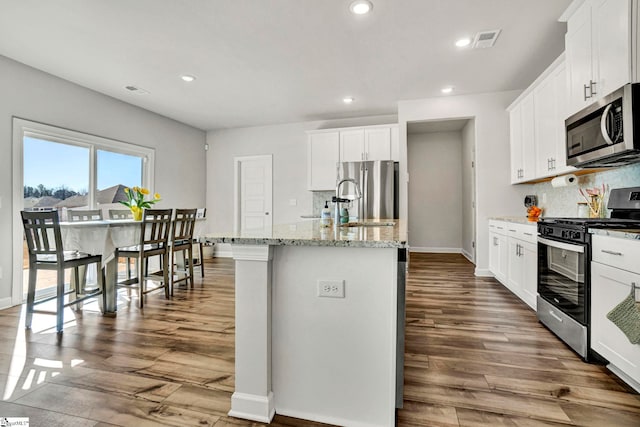 kitchen featuring light stone counters, dark wood finished floors, visible vents, appliances with stainless steel finishes, and an island with sink