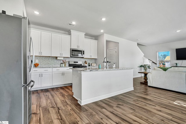 kitchen featuring stainless steel appliances, wood finished floors, visible vents, open floor plan, and backsplash