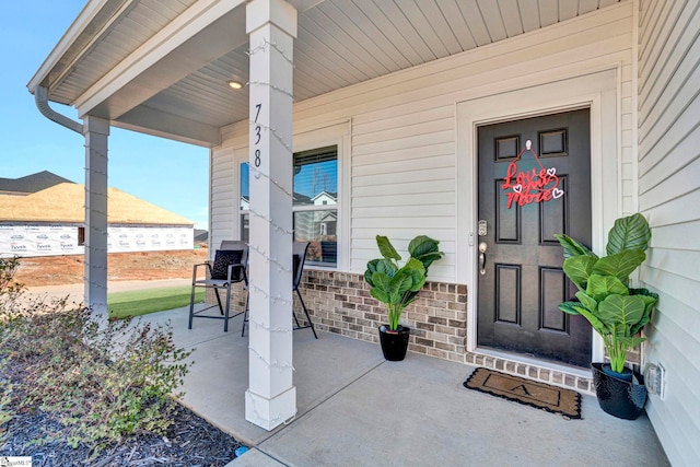 view of exterior entry featuring a porch and brick siding