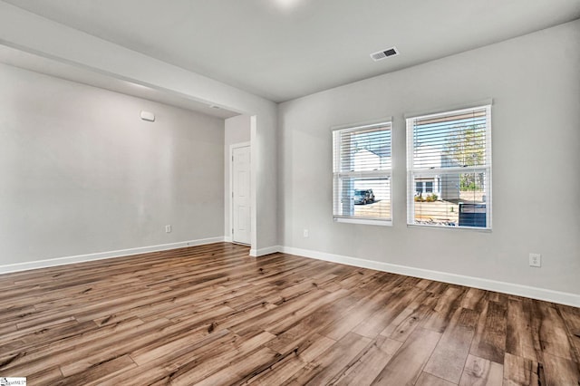 empty room with wood finished floors, visible vents, and baseboards