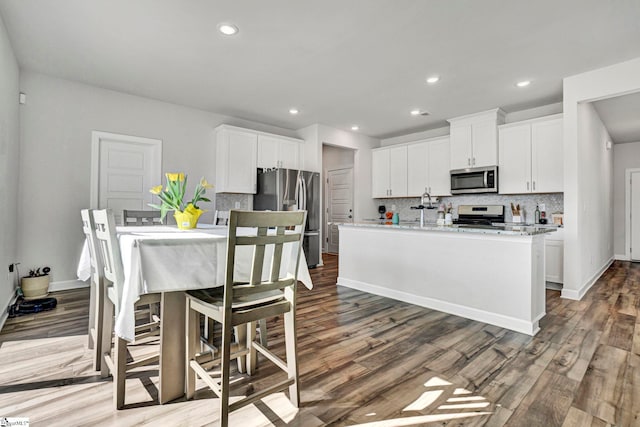 kitchen with appliances with stainless steel finishes, a kitchen island with sink, white cabinets, and backsplash