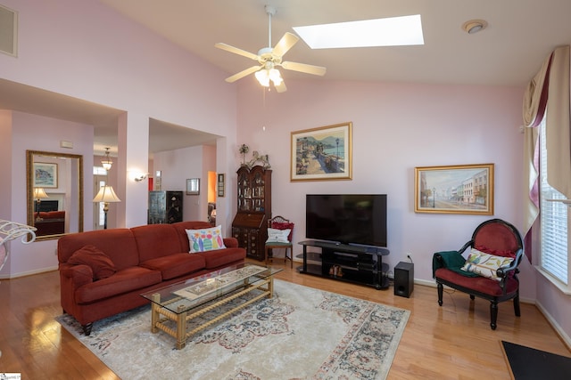 living area with vaulted ceiling with skylight, light wood-type flooring, a ceiling fan, and baseboards