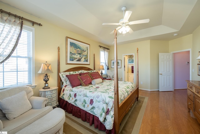 bedroom with multiple windows, a raised ceiling, light wood-style flooring, and baseboards