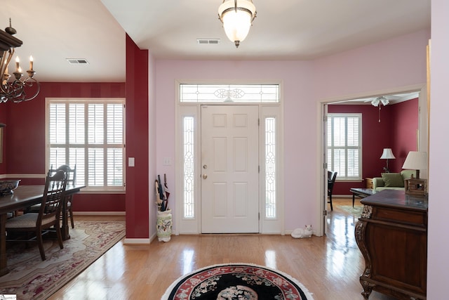 foyer entrance with light wood-style flooring, visible vents, a chandelier, and baseboards