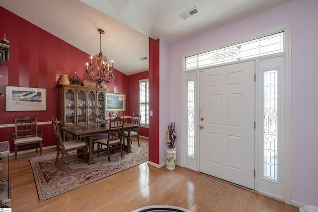 foyer entrance featuring baseboards, visible vents, lofted ceiling, wood finished floors, and a notable chandelier