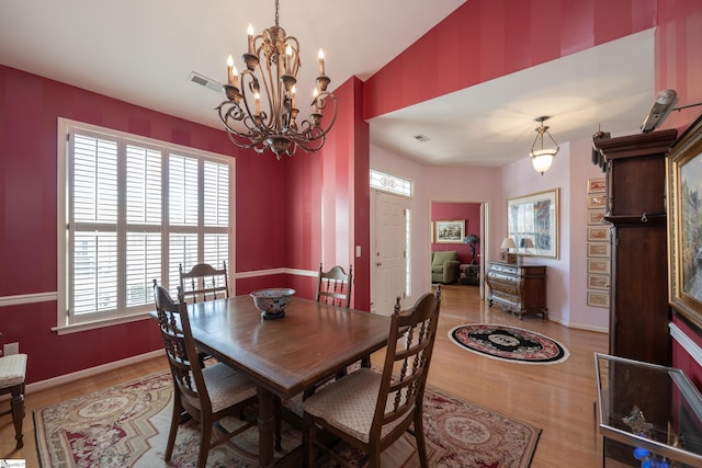 dining area with a chandelier, visible vents, baseboards, vaulted ceiling, and light wood-style floors