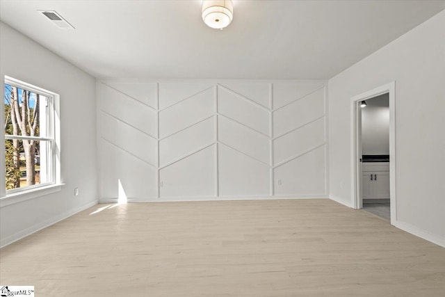 empty room with baseboards, light wood-type flooring, visible vents, and a decorative wall