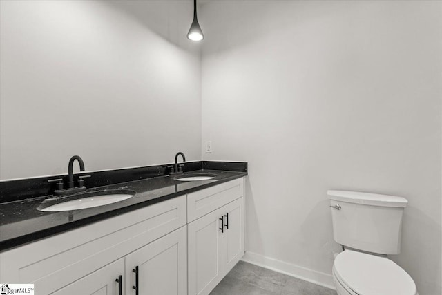 bathroom featuring toilet, double vanity, baseboards, and a sink