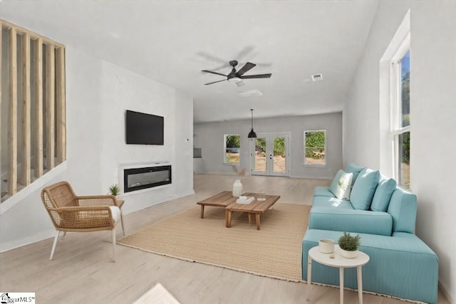 living area with ceiling fan, wood finished floors, a glass covered fireplace, and visible vents