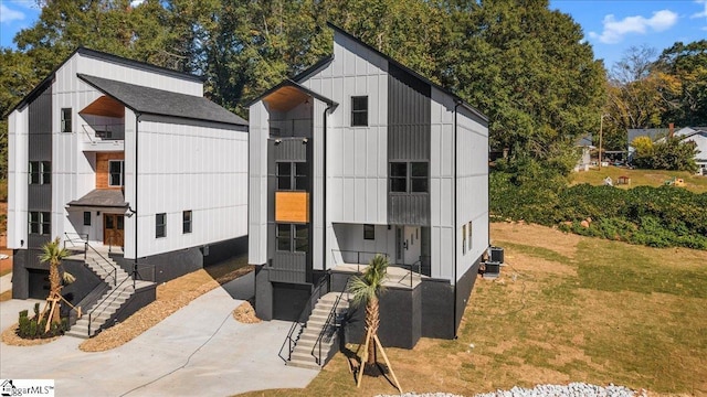 view of front facade featuring board and batten siding, a front lawn, and central AC